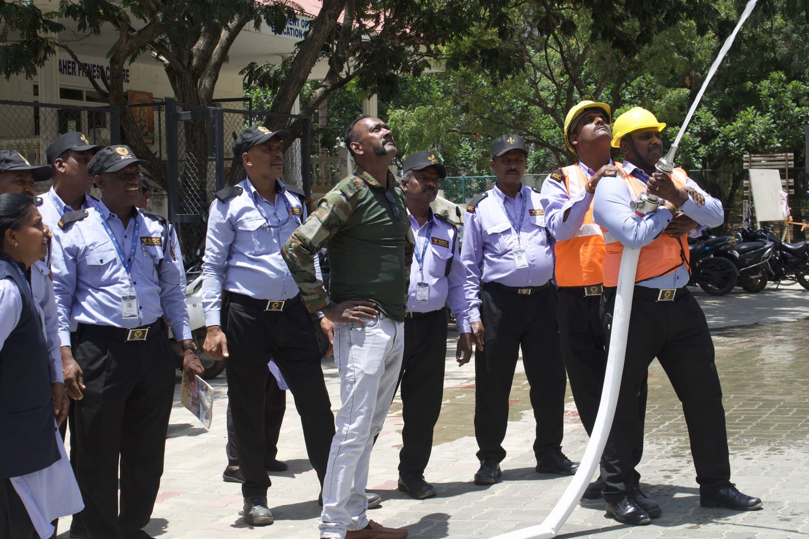 SDC guards in yellow helmets raising a fire hose during a drill as colleagues watch